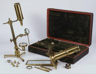 A microscope compendium containing many different parts in a portable case; microscopes are shown assembled in the foreground.